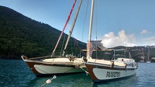 The Mahiya catamaran moored in a calm turquoise bay with lush green VI hillside behind, MAHIYA name on hull