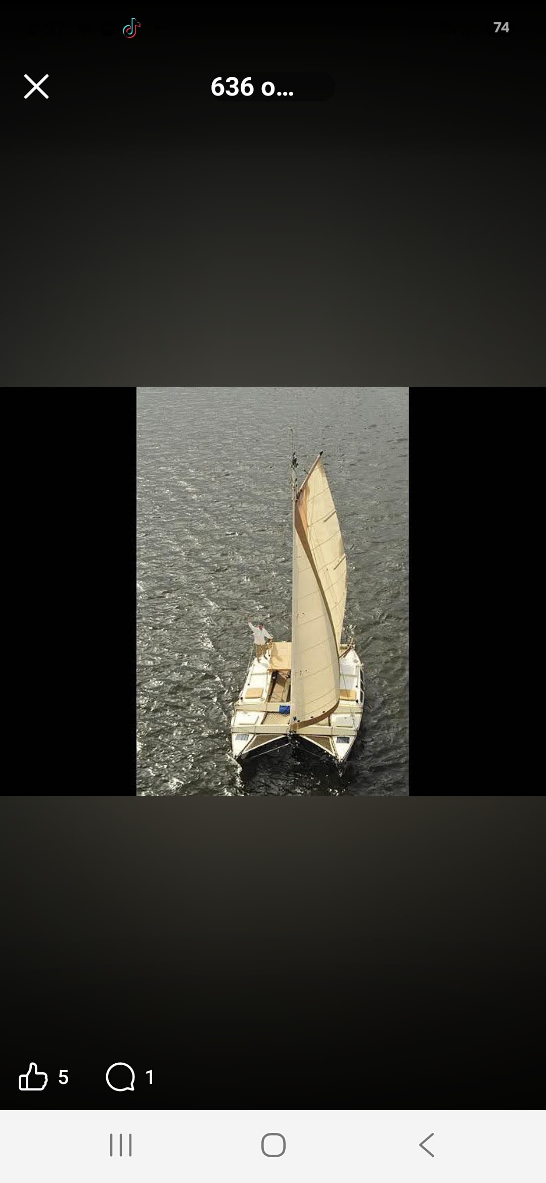 Aerial drone shot of the Mahiya catamaran under sail on choppy grey water, Captain Karl waving from the bow