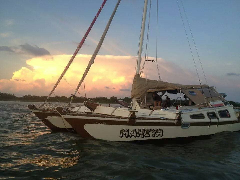 The Mahiya catamaran moored at dusk with MAHIYA name on the hull, dramatic golden and purple storm clouds behind