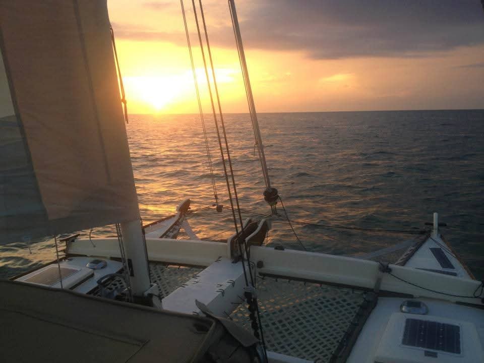 View from the Mahiya deck looking forward at a golden sunset over the open Caribbean sea, solar panels and rigging visible